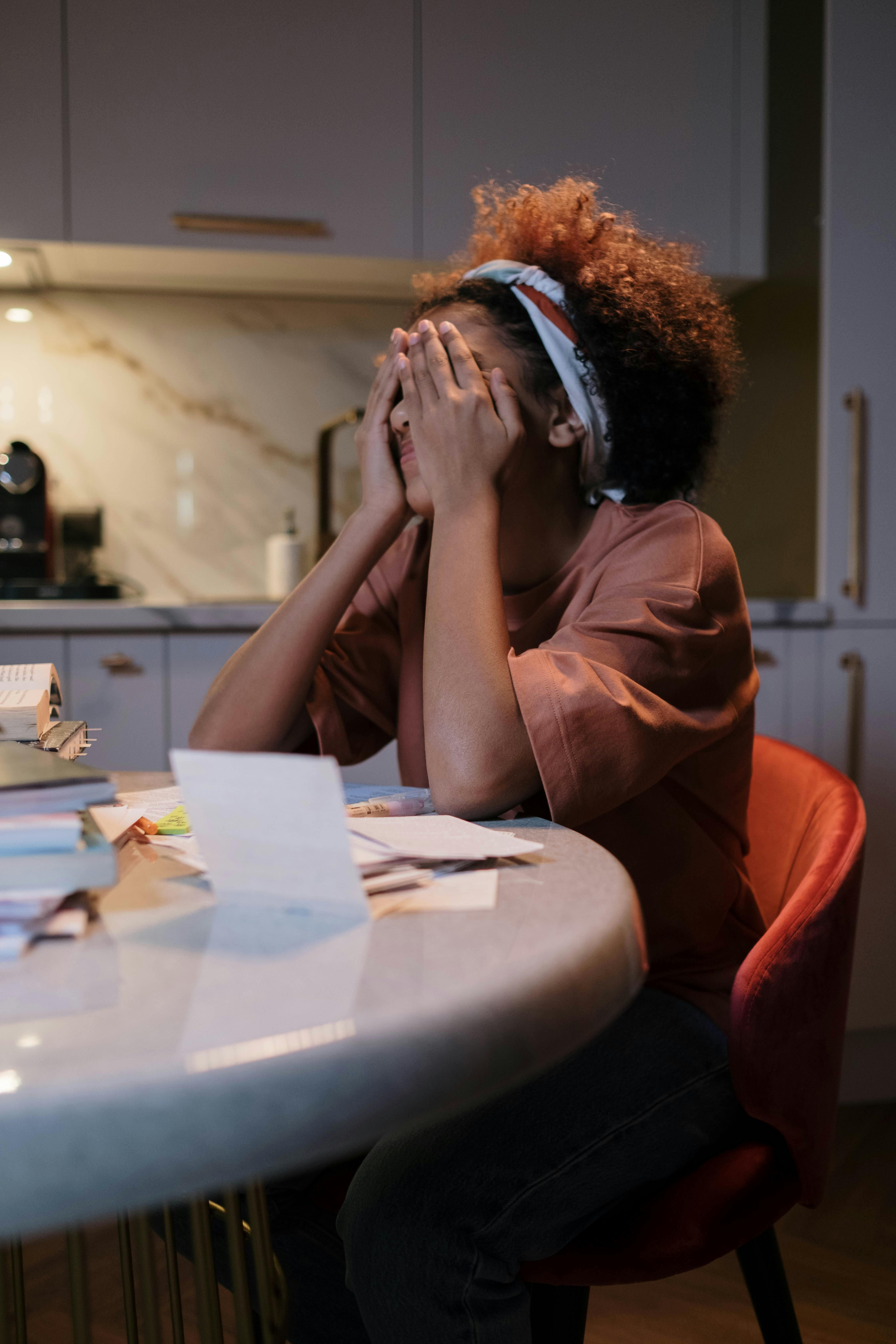 overwhelmed mom sitting at kitchen table representing the mental load of parenting and being the default parent